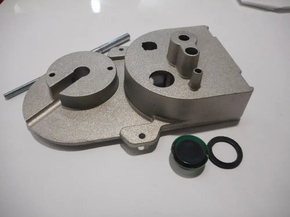 Luftgehäuse von Remeha, aus Metall, mit mehreren Öffnungen und einer abgerundeten Form. Zwei Dichtungen und eine Gewindestange liegen daneben.